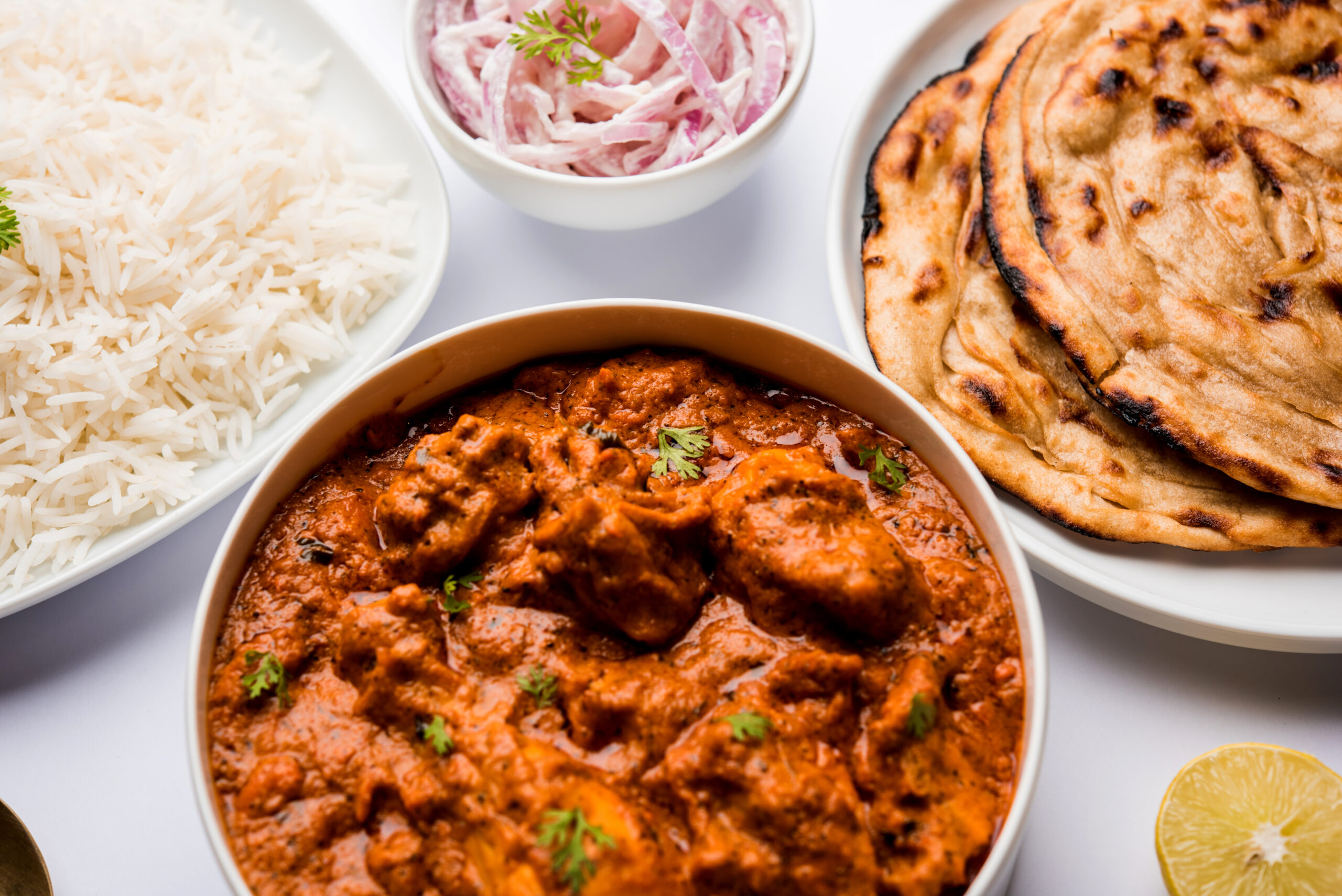 Murgh Makhani or Butter chicken tikka masala served with roti or Paratha and plain rice along with onion salad in terracotta crockery. selective focus